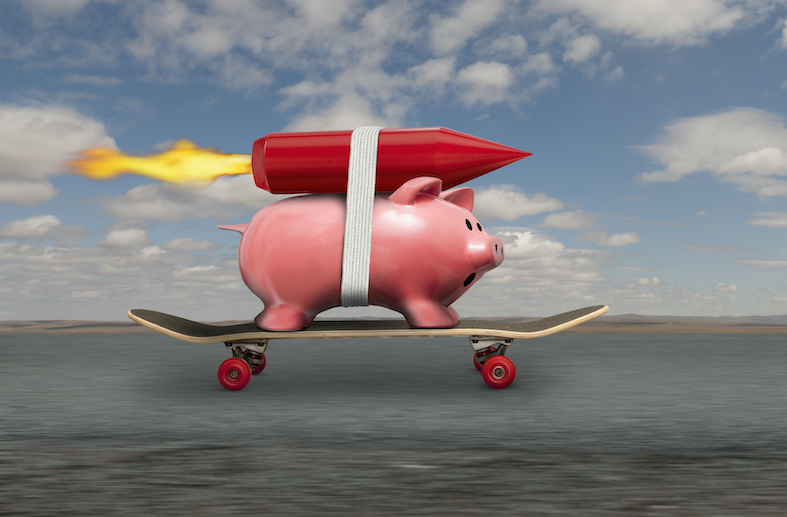 A piggy bank streaks down the road to riches on a skateboard and with a rocket strapped to his back.