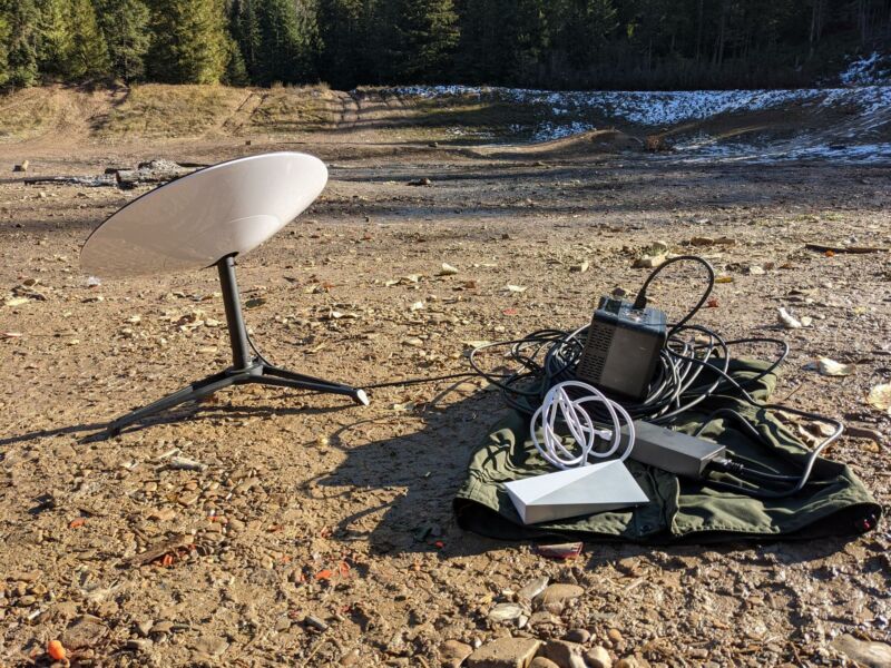 A Starlink satellite dish sits on the ground in a clearing in the middle of a forest.