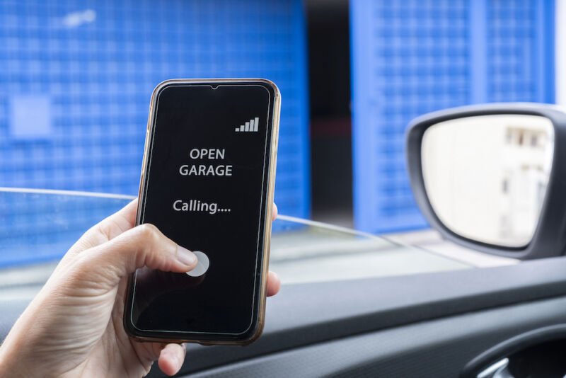 woman inside the car using mobile phone to open garage. woman entering pin into smartphone while unlocking garage.