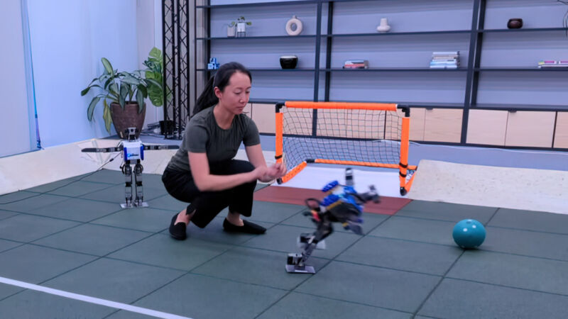 In a still from a DeepMind demo video, a researcher pushes a small humanoid robot to the ground.