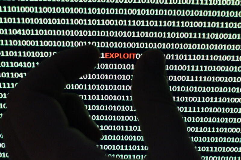 Photograph depicts a security scanner extracting virus from a string of binary code. Hand with the word "exploit"