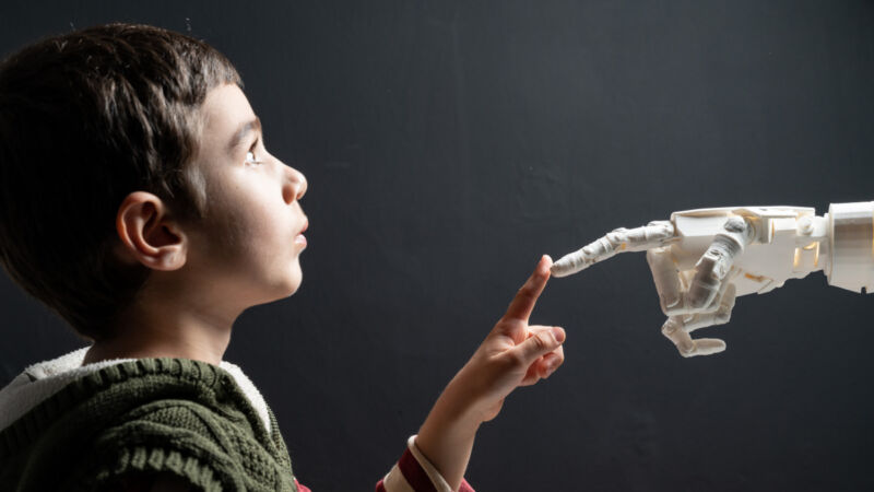 An elementary-school-aged child touching a robot hand.